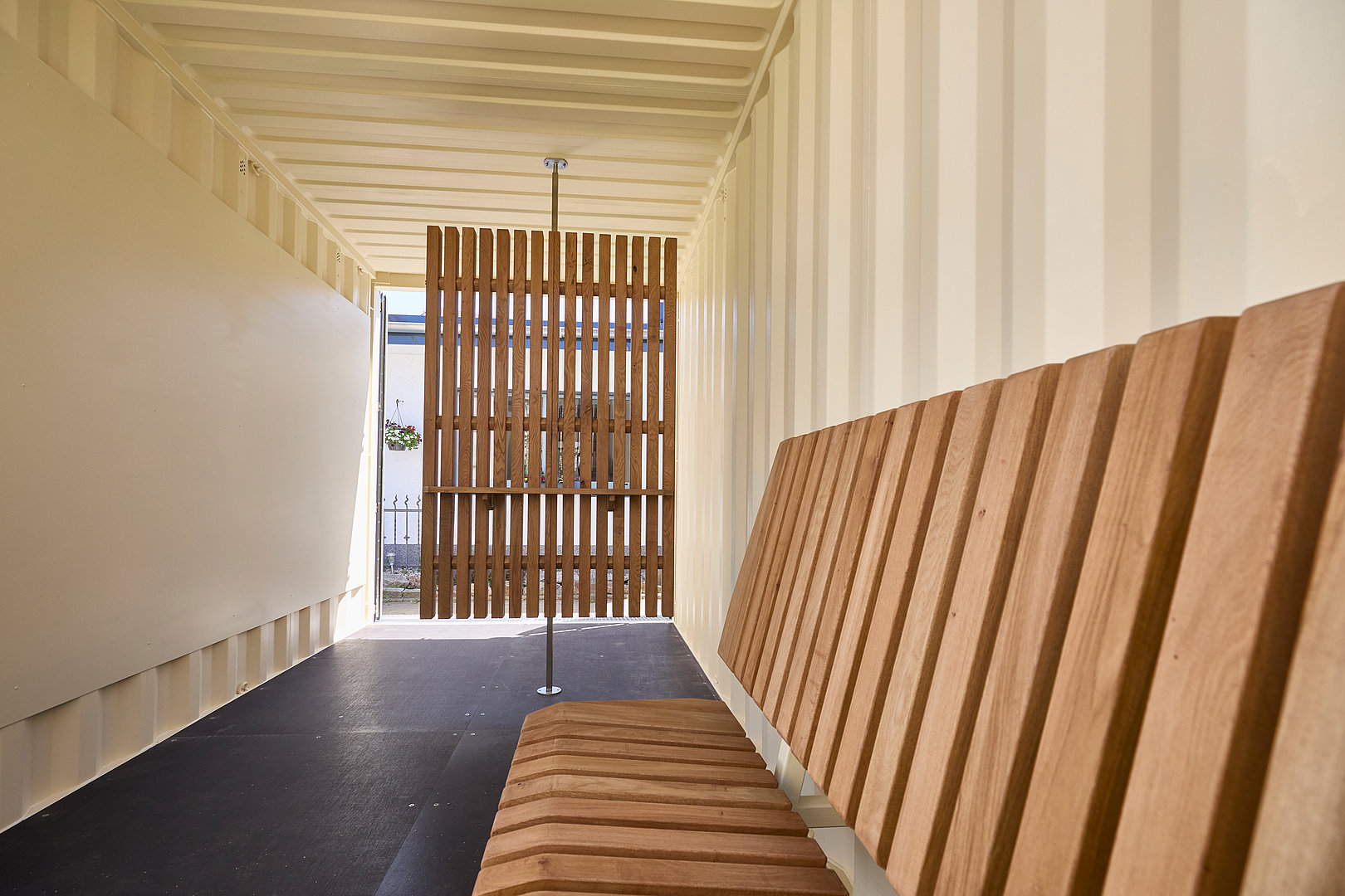 Blick durch den Container mit Holzbank und Lamellenwand